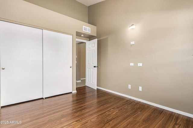 unfurnished bedroom featuring wood finished floors, visible vents, a closet, and baseboards