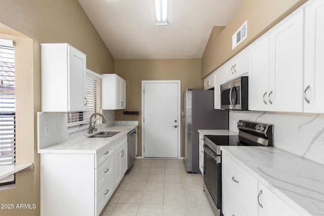 kitchen with tasteful backsplash, light stone countertops, appliances with stainless steel finishes, white cabinets, and a sink