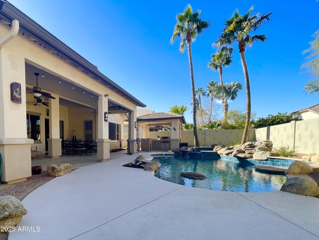 view of swimming pool featuring an outdoor kitchen, exterior bar, an in ground hot tub, ceiling fan, and a patio area