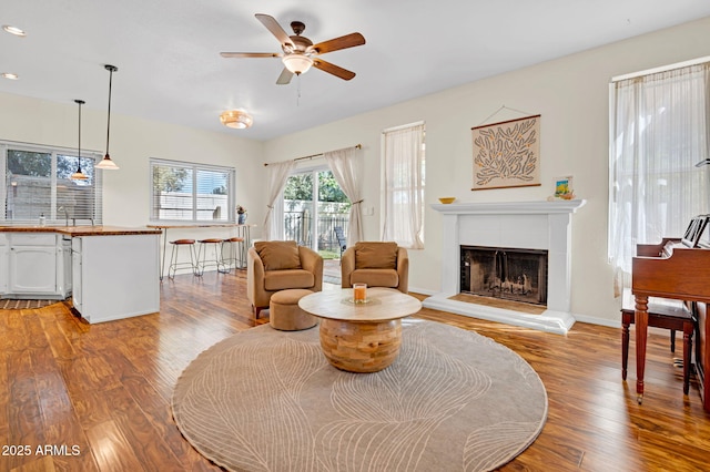 living room featuring light wood-style floors, ceiling fan, recessed lighting, a tile fireplace, and baseboards