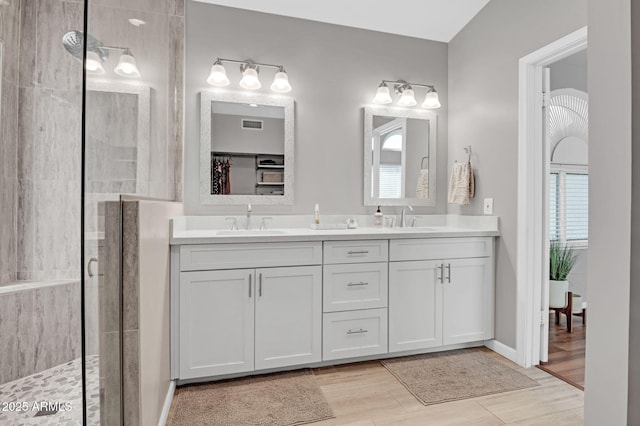 full bath featuring a tile shower, double vanity, wood finished floors, and a sink