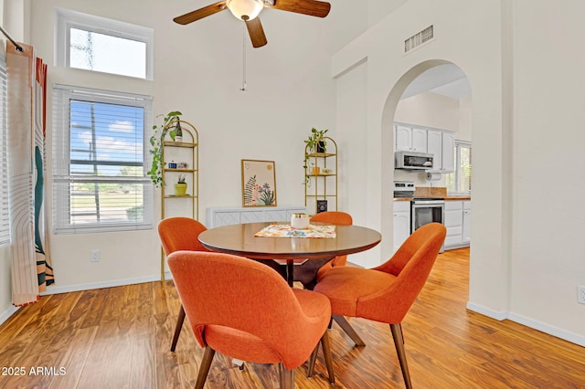 dining space with a towering ceiling, a wealth of natural light, visible vents, ceiling fan, and arched walkways