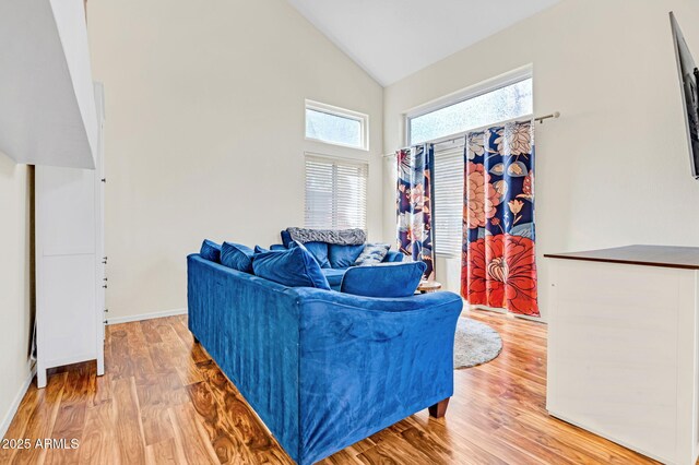 living area featuring baseboards, light wood-style flooring, and high vaulted ceiling