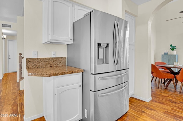 kitchen with stainless steel fridge, arched walkways, light wood finished floors, white cabinets, and baseboards