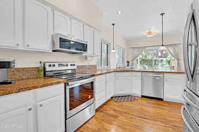 kitchen with white cabinets, hanging light fixtures, stainless steel appliances, and a sink