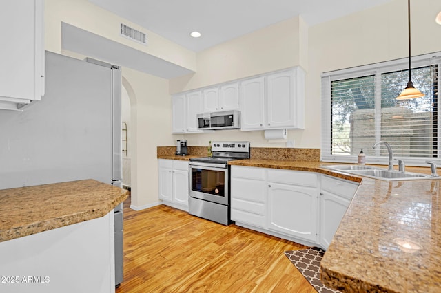 kitchen with visible vents, a sink, arched walkways, light wood-type flooring, and appliances with stainless steel finishes