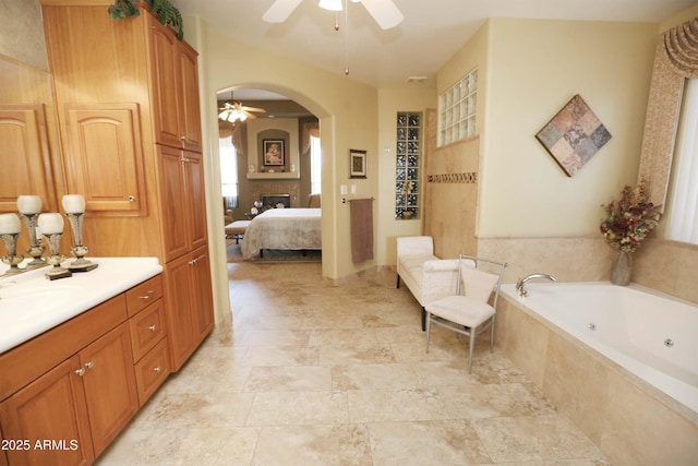 bathroom featuring vanity, tiled tub, a fireplace, and ceiling fan