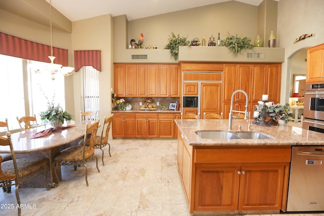 kitchen with appliances with stainless steel finishes, high vaulted ceiling, decorative light fixtures, sink, and a kitchen island with sink