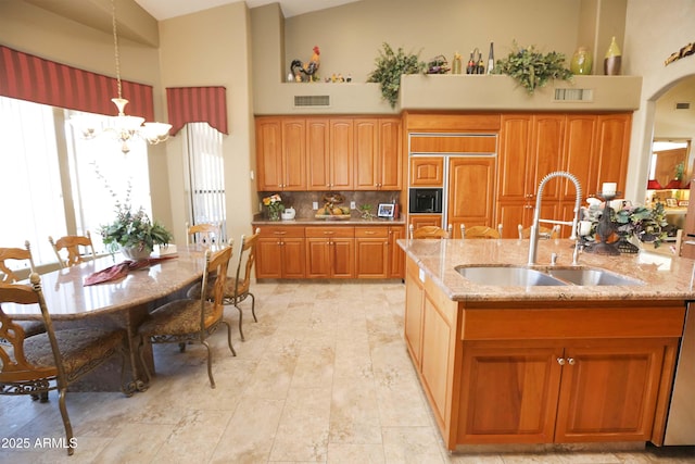 kitchen featuring sink, light stone counters, decorative light fixtures, paneled refrigerator, and a towering ceiling