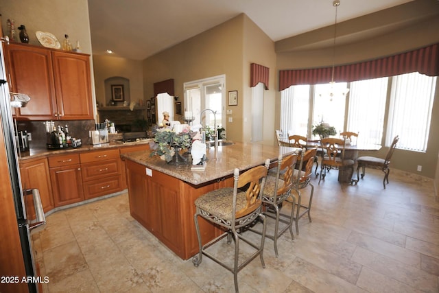 kitchen with sink, decorative light fixtures, an island with sink, light stone countertops, and decorative backsplash