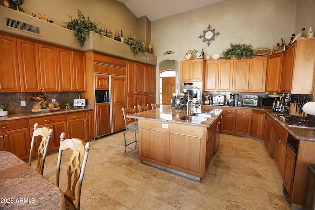 kitchen with sink, stainless steel appliances, an island with sink, and high vaulted ceiling