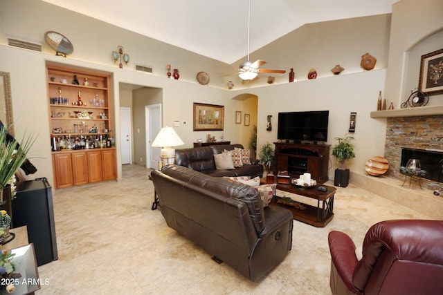 living room with high vaulted ceiling, a fireplace, ceiling fan, bar area, and built in shelves