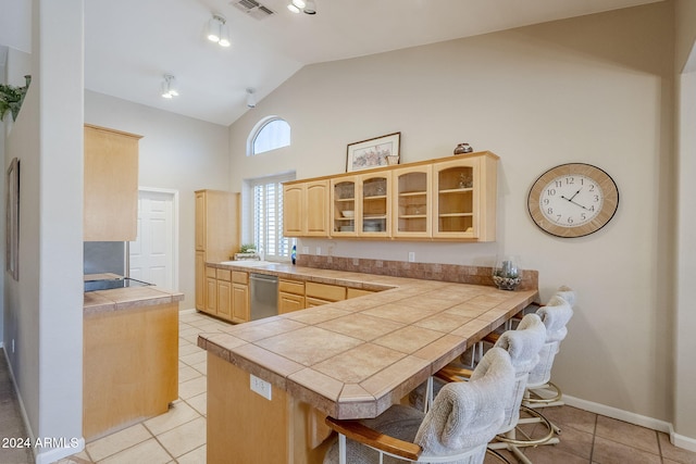 kitchen featuring dishwasher, kitchen peninsula, lofted ceiling, a breakfast bar area, and light tile patterned flooring