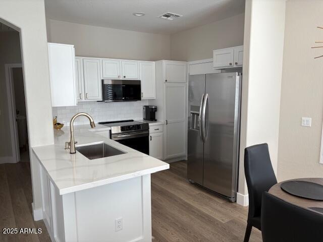 kitchen with sink, appliances with stainless steel finishes, dark hardwood / wood-style flooring, kitchen peninsula, and white cabinets