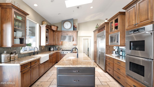 kitchen featuring sink, vaulted ceiling with skylight, built in appliances, an island with sink, and decorative backsplash