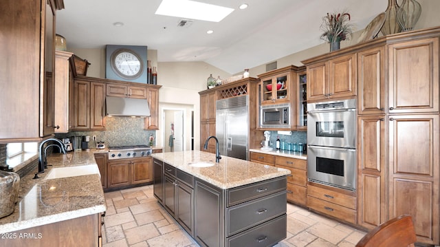 kitchen with built in appliances, sink, light stone countertops, and an island with sink