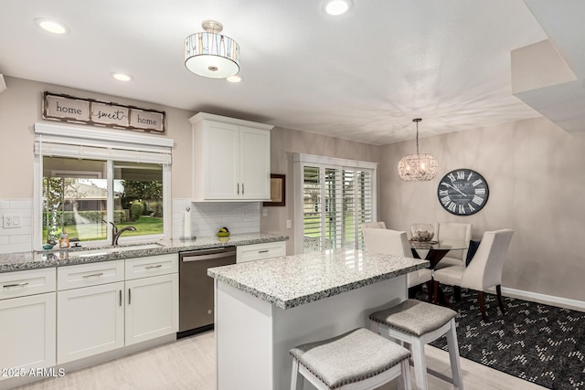 kitchen featuring pendant lighting, white cabinetry, sink, stainless steel dishwasher, and light stone counters