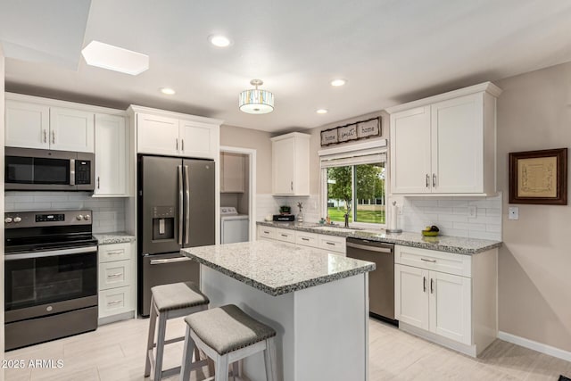 kitchen featuring appliances with stainless steel finishes, a kitchen island, washer / clothes dryer, light stone countertops, and white cabinets