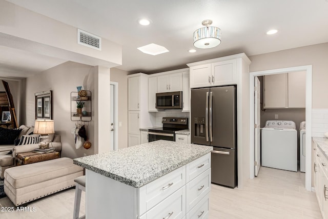 kitchen with white cabinetry, stainless steel appliances, washing machine and clothes dryer, a kitchen island, and decorative backsplash