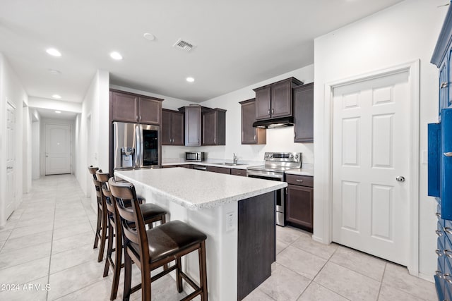 kitchen with sink, a center island, appliances with stainless steel finishes, a breakfast bar area, and light tile patterned flooring