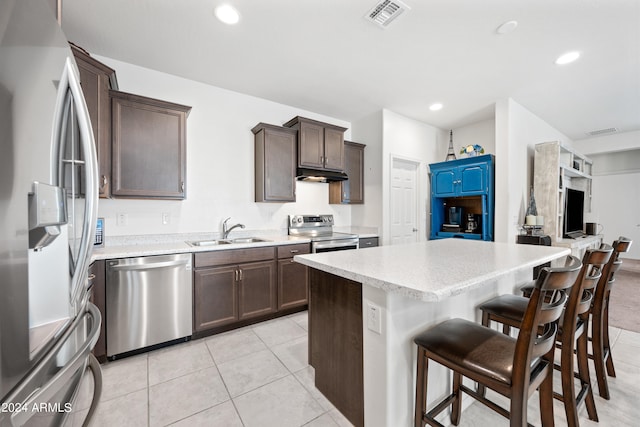 kitchen with appliances with stainless steel finishes, sink, light tile patterned flooring, a kitchen island, and a breakfast bar