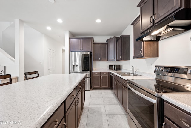 kitchen featuring custom exhaust hood, light tile patterned floors, sink, appliances with stainless steel finishes, and dark brown cabinetry