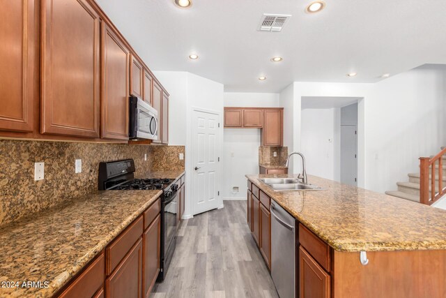 kitchen featuring backsplash, stainless steel appliances, light hardwood / wood-style flooring, sink, and an island with sink