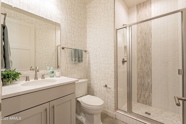 bathroom with vanity, toilet, tile walls, a stall shower, and tile patterned floors