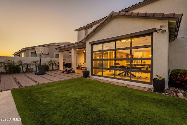 rear view of house with stucco siding, a lawn, a patio area, fence, and a tile roof