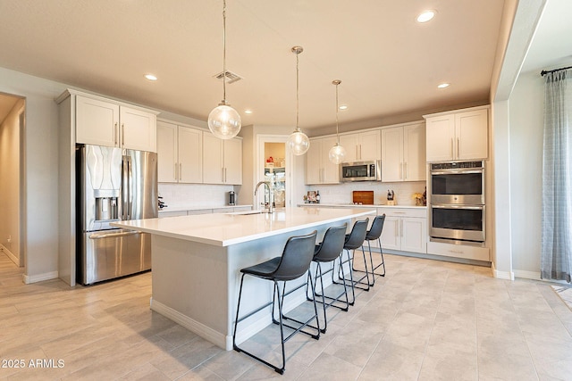kitchen featuring visible vents, a sink, light countertops, appliances with stainless steel finishes, and a kitchen island with sink