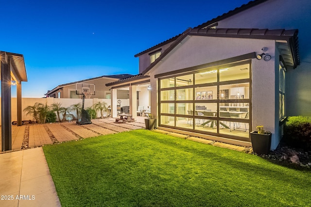 rear view of property with a patio area, stucco siding, fence, and a lawn