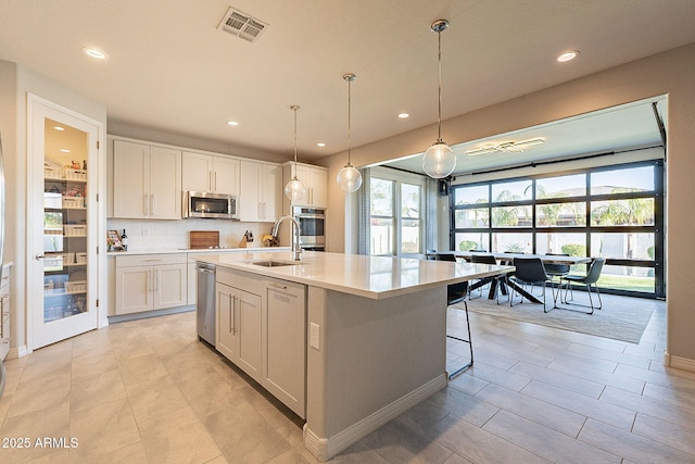 kitchen featuring visible vents, a sink, light countertops, an island with sink, and stainless steel microwave