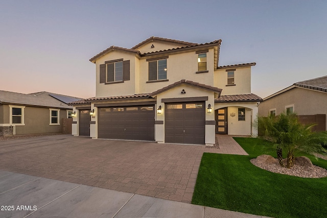 mediterranean / spanish home with stucco siding, decorative driveway, an attached garage, and a tile roof