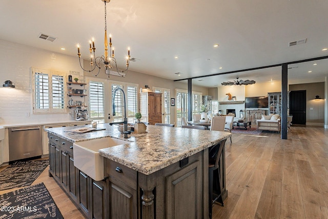 kitchen featuring light stone counters, dark brown cabinets, a center island with sink, an inviting chandelier, and dishwasher