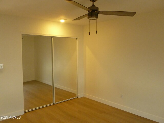 unfurnished bedroom with ceiling fan, a closet, baseboards, and wood finished floors