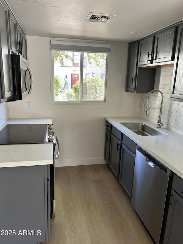 kitchen featuring visible vents, light wood finished floors, a sink, stainless steel appliances, and light countertops