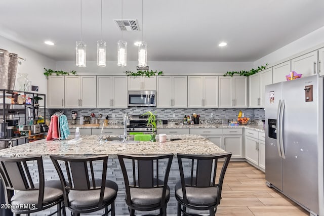 kitchen featuring white cabinetry, tasteful backsplash, hanging light fixtures, appliances with stainless steel finishes, and an island with sink