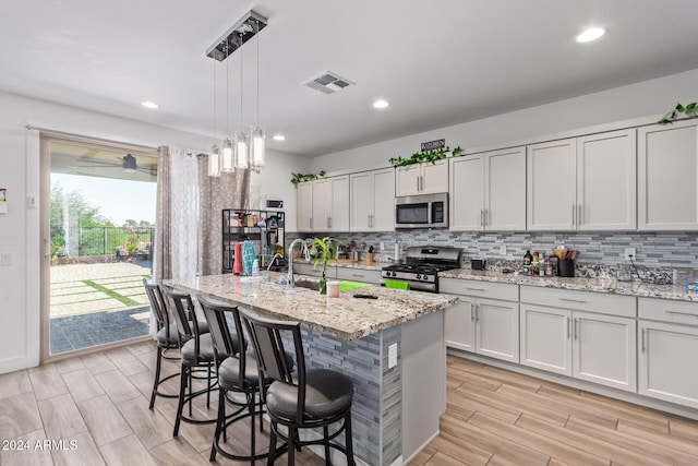 kitchen with a center island with sink, pendant lighting, stainless steel appliances, light stone countertops, and backsplash