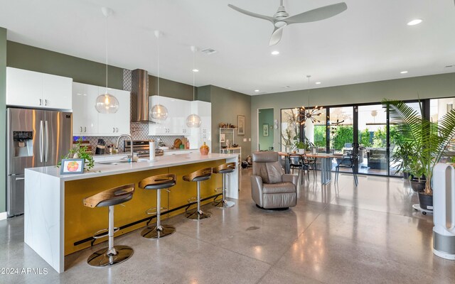 kitchen featuring appliances with stainless steel finishes, white cabinets, a kitchen bar, decorative light fixtures, and wall chimney range hood