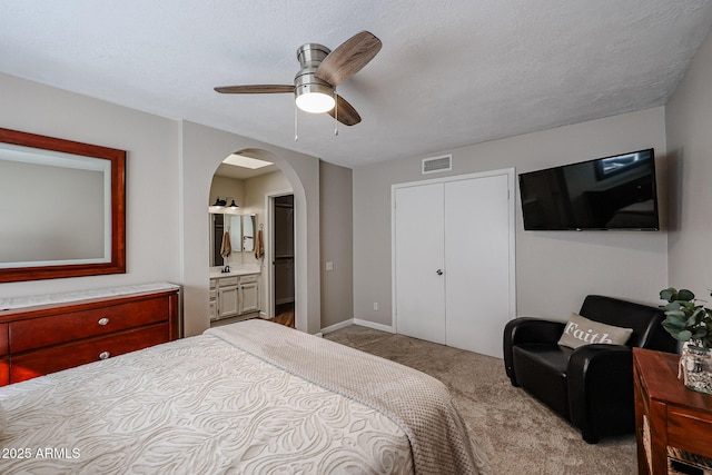 bedroom featuring light carpet, connected bathroom, a textured ceiling, and ceiling fan