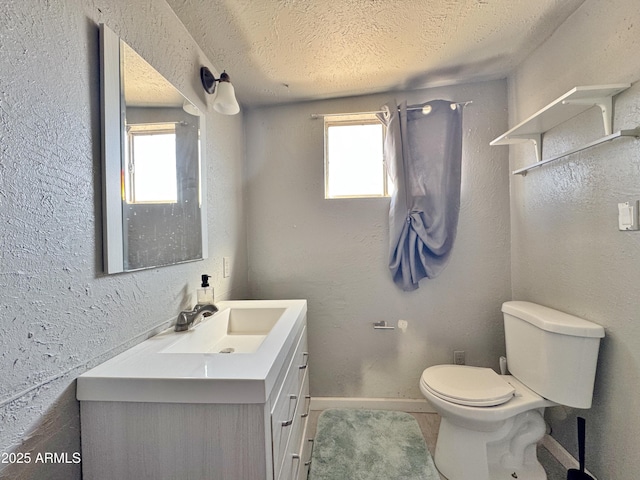 bathroom with vanity, a textured ceiling, toilet, and a healthy amount of sunlight