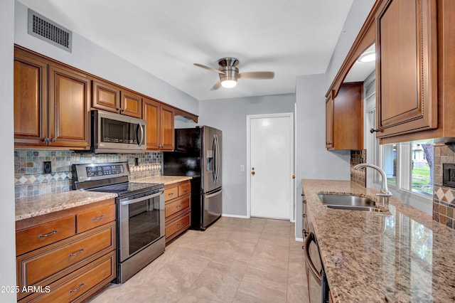 kitchen featuring visible vents, a sink, decorative backsplash, ceiling fan, and stainless steel appliances