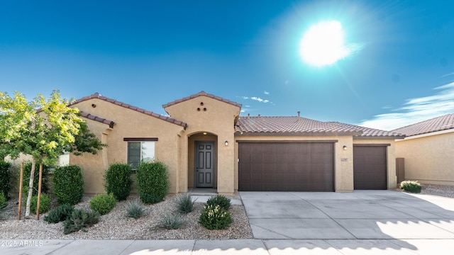 mediterranean / spanish-style home with an attached garage, stucco siding, a tiled roof, and concrete driveway