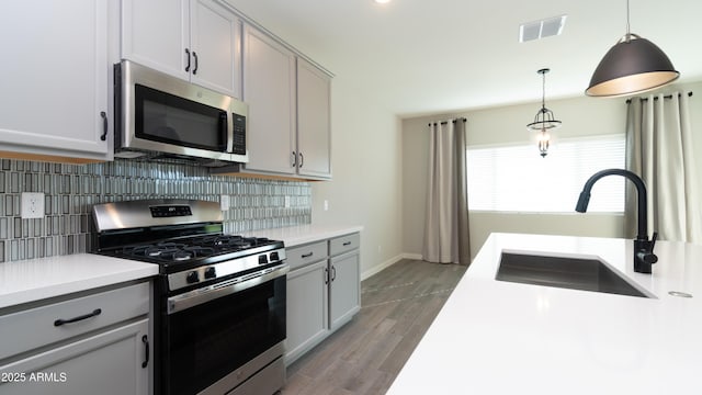 kitchen with a sink, gray cabinets, stainless steel appliances, backsplash, and visible vents