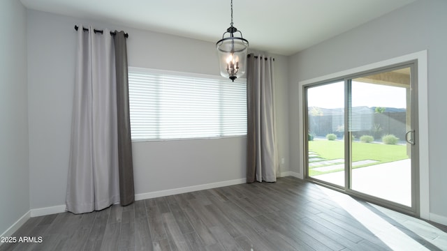 unfurnished dining area featuring baseboards, wood finished floors, and a notable chandelier
