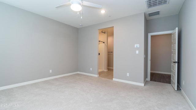 unfurnished bedroom featuring baseboards, a walk in closet, light colored carpet, and visible vents