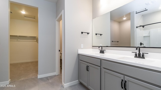 bathroom featuring a sink, baseboards, double vanity, and a spacious closet