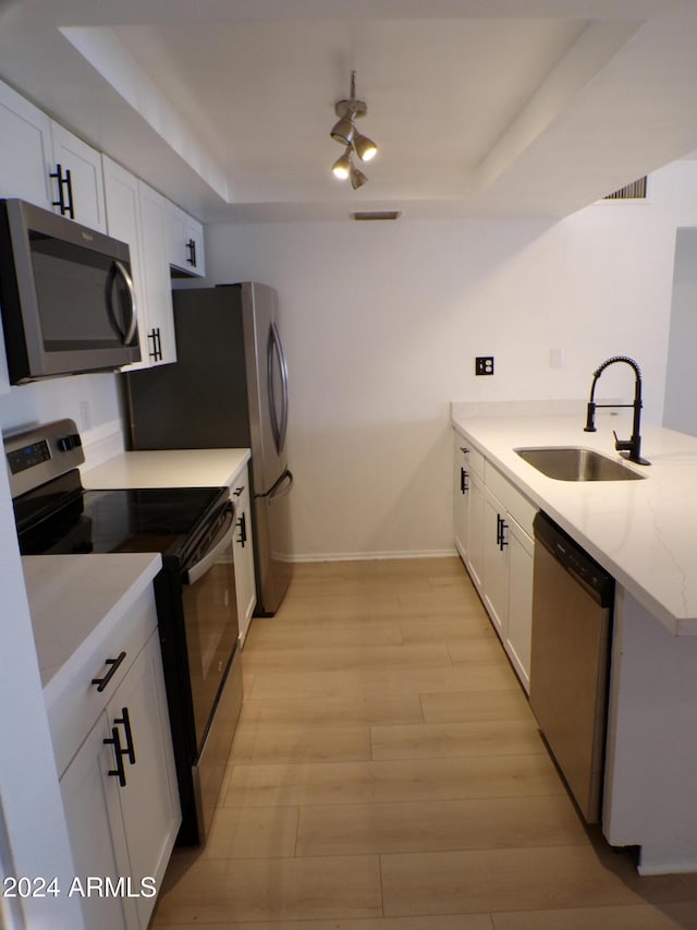 kitchen with sink, a raised ceiling, appliances with stainless steel finishes, white cabinets, and light wood-type flooring