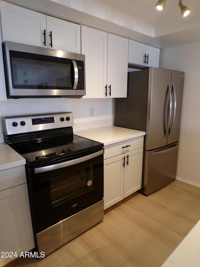 kitchen with stainless steel appliances, white cabinetry, and light hardwood / wood-style floors