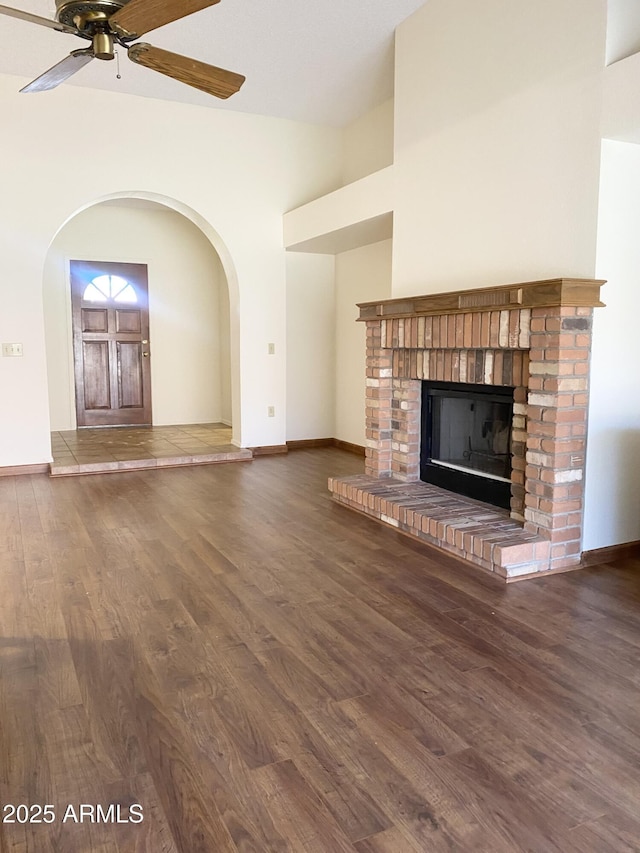 1249 E Commerce Ave, Gilbert, AZ 85234 - unfurnished living room featuring wood finished floors, a ceiling fan, a brick fireplace, arched walkways, and lofted ceiling